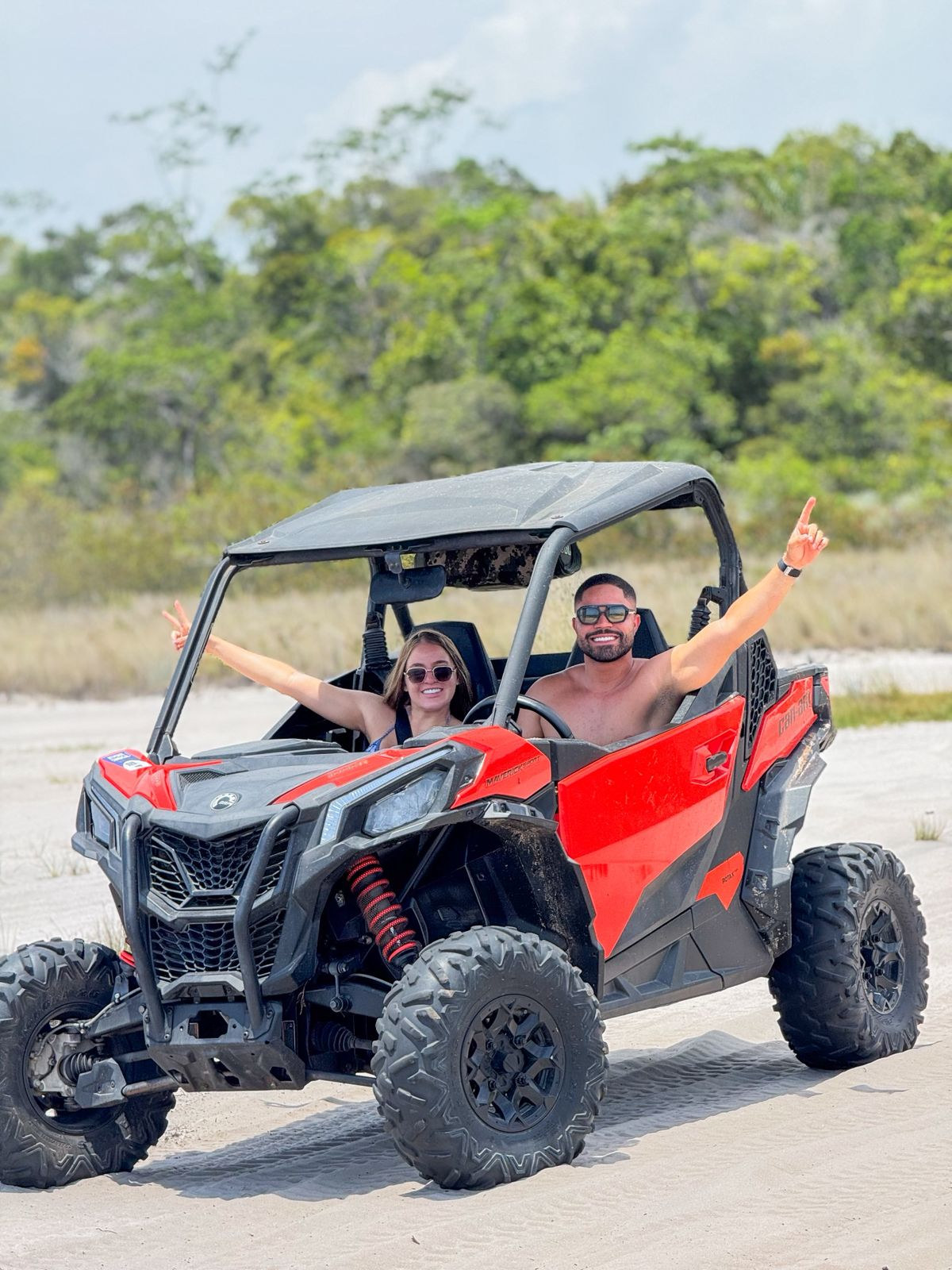 Casal comemorando a bordo de um UTV vermelho em trilha de areia